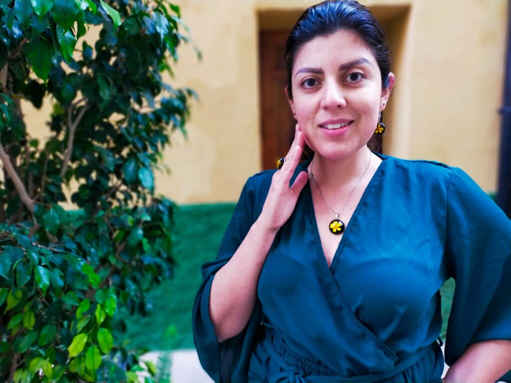 Mujer sonriendo con un jardín de fondo luciendo un conjunto de joyería floral, anillo, pendientes y colgante hechos a mano en resina epóxica y flores